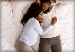 A couple lays on the bed together. The woman is pregnant.